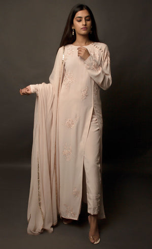 Dusty Rose side slit suit set, crafted in georgette, fully embroidered with signature flat threadwork topped with sequins spray accompanied by a dupatta with rose gold mukaish border. The ensemble carries a strong of a confident style because of the slim straight trousers underneath, the bottom of the trousers is finished by our signature buttoned hemline style. Flaunt your chic style in this elaborately worked ensemble, the muse radiates a modern, yet classic vibe.