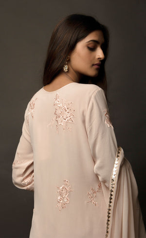 Dusty Rose side slit suit set, crafted in georgette, fully embroidered with signature flat threadwork topped with sequins spray accompanied by a dupatta with rose gold mukaish border. The ensemble carries a strong of a confident style because of the slim straight trousers underneath, the bottom of the trousers is finished by our signature buttoned hemline style. Flaunt your chic style in this elaborately worked ensemble, the muse radiates a modern, yet classic vibe.