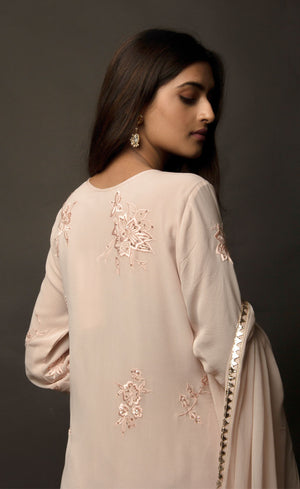 Dusty Rose side slit suit set, crafted in georgette, fully embroidered with signature flat threadwork topped with sequins spray accompanied by a dupatta with rose gold mukaish border. The ensemble carries a strong of a confident style because of the slim straight trousers underneath, the bottom of the trousers is finished by our signature buttoned hemline style. Flaunt your chic style in this elaborately worked ensemble, the muse radiates a modern, yet classic vibe. 