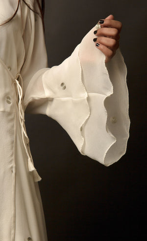 The muse is seen here wearing a classic angrakha style kurta suit set, delicately hand embroidered with a steel grey tilla. The motifs are scattered all over the front and back of this ivory angrakha set in georgette. The double bell sleeve with a beautiful flare, is a little modern play here in this classic angrakha silhouette. The silhouette is paired with wide legged easy palazzos and a dupatta embellished with tonal grey beadwork border.