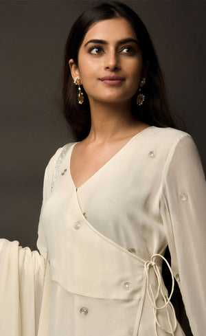 The muse is seen here wearing a classic angrakha style kurta suit set, delicately hand embroidered with a steel grey tilla. The motifs are scattered all over the front and back of this ivory angrakha set in georgette. The double bell sleeve with a beautiful flare, is a little modern play here in this classic angrakha silhouette. The silhouette is paired with wide legged easy palazzos and a dupatta embellished with tonal grey beadwork border.