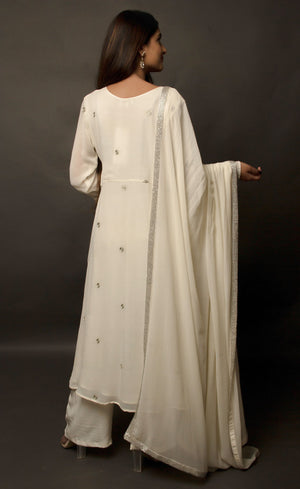 The muse is seen here wearing a classic angrakha style kurta suit set, delicately hand embroidered with a steel grey tilla. The motifs are scattered all over the front and back of this ivory angrakha set in georgette. The double bell sleeve with a beautiful flare, is a little modern play here in this classic angrakha silhouette. The silhouette is paired with wide legged easy palazzos and a dupatta embellished with tonal grey beadwork border.
