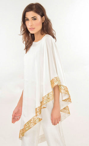 The muse here is wearing our effortlessly elegant ivory cape dress. This is a silk asymmetrical one shoulder cape which is intricately embroidered with sequins along the flowy flared border of the cape, which is further paired with straight trousers with metal buttons finishing on the bottom cuff sides. Perfect for every occasion, this stunning outfit will make you dazzle and look your best.