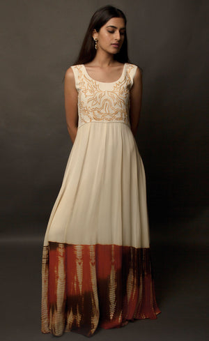 This particular ivory dress in georgette carries a series of thin beautiful long floor length panels from waist down, the yoke is embroidered with a rust colour thread-work, the front and back of the yoke is embroidered with an intentional different pattern, the back yoke embroidery is more prominent and dense than the front. The knee down has been treated with hand tie and dye Batik technique in deep rust and brown accents over the ivory base. 