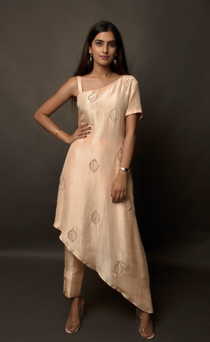 The muse is seen wearing a beautiful asymmetrical flared dress in powder peach. There is a traditional mango motif crafted in glass beads all over the front and the back of the dress. Little details like the anchor thread-work over the small strap are intricate details that only a wearer can enjoy. This ankle length dress is perfectly paired with our signature buttoned pants. This glamorous outfit with these enhanced elements is a perfect outfit for any event.