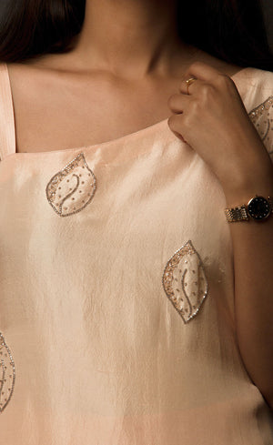 The muse is seen wearing a beautiful asymmetrical flared dress in powder peach. There is a traditional mango motif crafted in glass beads all over the front and the back of the dress. Little details like the anchor thread-work over the small strap are intricate details that only a wearer can enjoy. This ankle length dress is perfectly paired with our signature buttoned pants. This glamorous outfit with these enhanced elements is a perfect outfit for any event.