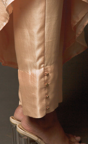 The muse is seen wearing a beautiful asymmetrical flared dress in powder peach. There is a traditional mango motif crafted in glass beads all over the front and the back of the dress. Little details like the anchor thread-work over the small strap are intricate details that only a wearer can enjoy. This ankle length dress is perfectly paired with our signature buttoned pants. This glamorous outfit with these enhanced elements is a perfect outfit for any event.
