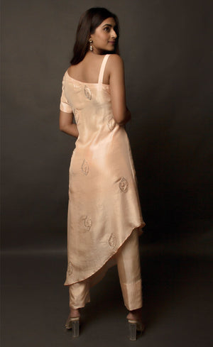 The muse is seen wearing a beautiful asymmetrical flared dress in powder peach. There is a traditional mango motif crafted in glass beads all over the front and the back of the dress. Little details like the anchor thread-work over the small strap are intricate details that only a wearer can enjoy. This ankle length dress is perfectly paired with our signature buttoned pants. This glamorous outfit with these enhanced elements is a perfect outfit for any event.