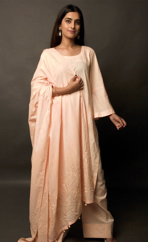 The muse here is wearing a peach embroidered kurta suit set. This is a 100% cotton suit with panelled kurta having lace insertions in the vertical panels and pin tucks in the upper yolk. The kurta is enhanced with flared sleeves having single horizontal lace insertion around the elbow. It is paired with a flared cotton palazzos and a cotton dupatta with our signature thread-work embroidery along its width, further finished with a buttoned detail. 