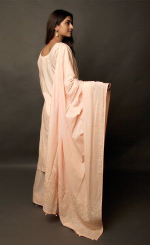 The muse here is wearing a peach embroidered kurta suit set. This is a 100% cotton suit with panelled kurta having lace insertions in the vertical panels and pin tucks in the upper yolk. The kurta is enhanced with flared sleeves having single horizontal lace insertion around the elbow. It is paired with a flared cotton palazzos and a cotton dupatta with our signature thread-work embroidery along its width, further finished with a buttoned detail.