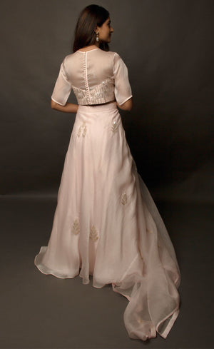 This dirty pale pink satin organza lehenga skirt is embroidered with zari and sequins motifs, the top is embellished with linear sequins and the coordinating silk organza dupatta is embroidered with sequin motifs finished with a raw silk border.