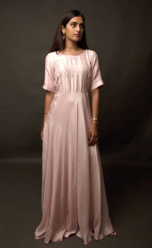 Graceful, demure and classic simplicity, this powder pink ensemble features a geometric hand embroidery on the mid yoke of this floor length flowing gown. Adorned with understated combination of peachy and translucent beads and threads, this cupro satin piece is yet a delicately detailed silhouette.