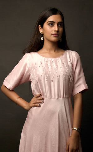 Graceful, demure and classic simplicity, this powder pink ensemble features a geometric hand embroidery on the mid yoke of this floor length flowing gown. Adorned with understated combination of peachy and translucent beads and threads, this cupro satin piece is yet a delicately detailed silhouette.