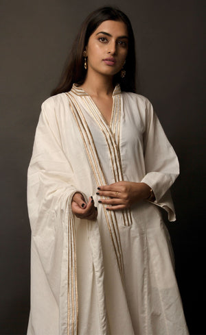 The muse is wearing a classic kurta set style, enhanced with added godet panels. This kurta is crafted in 100% cotton, is delicately embroidered with aari zari work paired with relaxed palazzos and accompanied by a 100% cotton dupatta embroidered with a coordinating zari border.