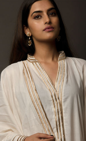 The muse is wearing a classic kurta set style, enhanced with added godet panels. This kurta is crafted in 100% cotton, is delicately embroidered with aari zari work paired with relaxed palazzos and accompanied by a 100% cotton dupatta embroidered with a coordinating zari border.