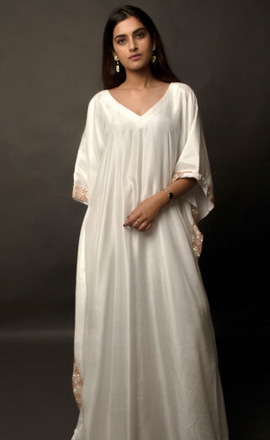 The muse is seen here wearing a classic V neck satin kaftan hand embellished with sequins and beads. The bordered embroidery beautifully runs along the length of the satin kaftan and also along its relaxed sleeves. The embellishments are all tonal shades of peach and off white.