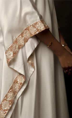 The muse is seen here wearing a classic V neck satin kaftan hand embellished with sequins and beads. The bordered embroidery beautifully runs along the length of the satin kaftan and also along its relaxed sleeves. The embellishments are all tonal shades of peach and off white.