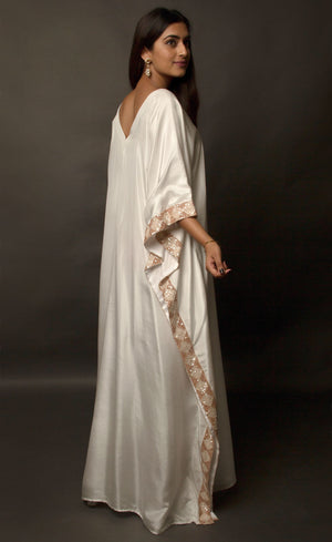 The muse is seen here wearing a classic V neck satin kaftan hand embellished with sequins and beads. The bordered embroidery beautifully runs along the length of the satin kaftan and also along its relaxed sleeves. The embellishments are all tonal shades of peach and off white.