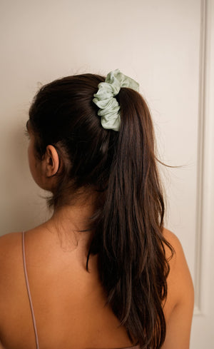 Person with a green scrunchie in their hair against a plain background
