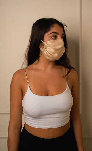 Woman wearing a white tank top and a beige face mask indoors.