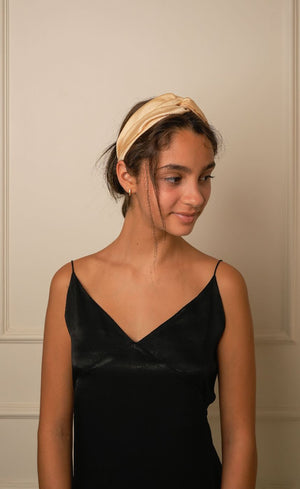 Woman wearing a black slip dress and beige headband against a neutral wall.