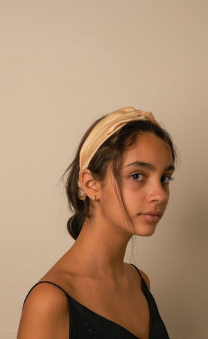 Beige satin knotted headband worn over hair, three-quarter side view