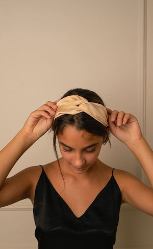 Woman tying Beige Bemberg satin knotted headband, front view with hands at hair