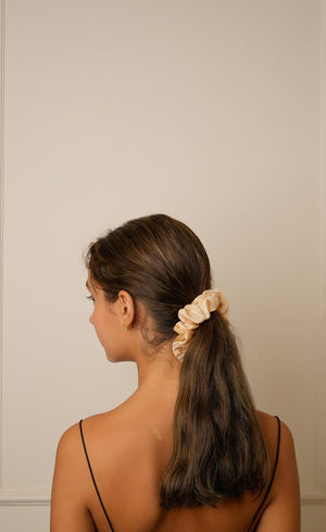 Woman with a ponytail wearing a beige scrunchie against a plain background