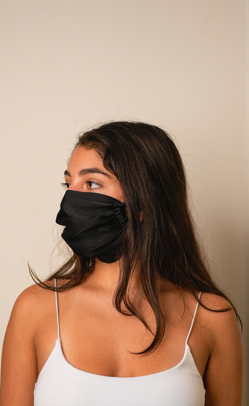 Woman wearing a black face mask against a beige background