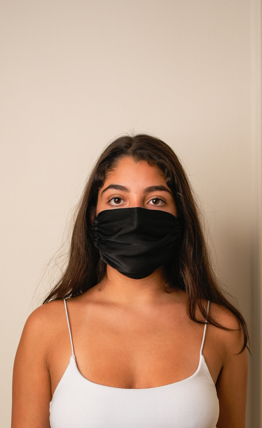 Woman wearing a black face mask against a beige background