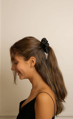 Woman with a ponytail wearing a black top against a beige wall