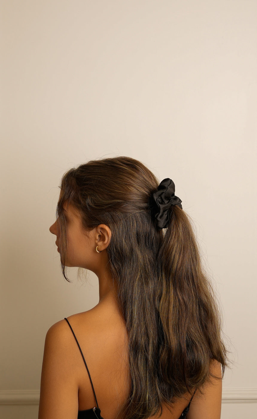 Woman with long hair tied back with a black scrunchie against a plain background