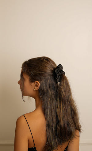 Woman with long hair tied back with a scrunchie against a plain wall