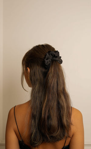 Woman with long hair tied back with a black scrunchie against a plain background