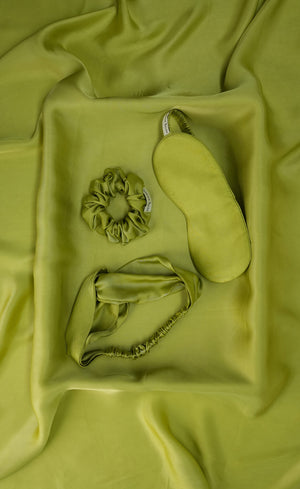 Set of green scrunchie, eye mask, and hair tie on a green fabric background