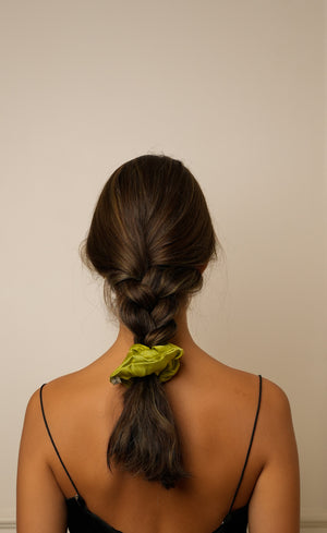 Person with a green scrunchie in their braided hair against a beige background
