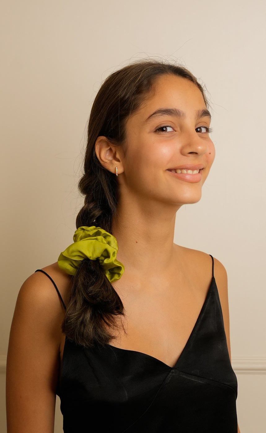 Young woman with a green scrunchie in her hair against a plain background