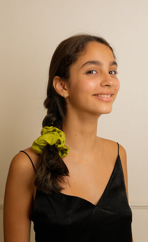 Young woman with a green scrunchie in her hair against a plain background