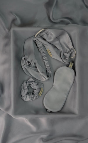 Grey sleep mask and earbuds on a textured grey fabric background
