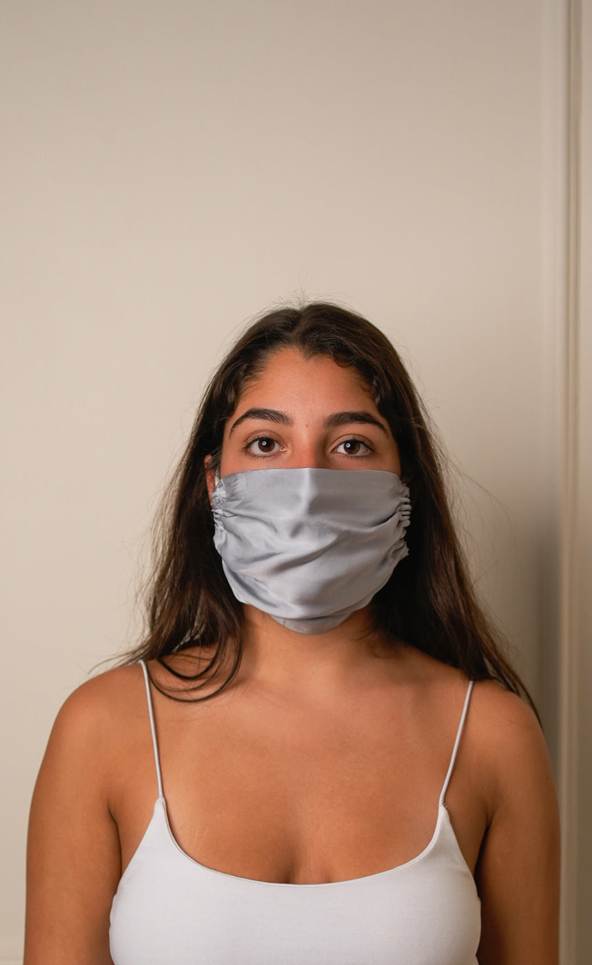 Woman wearing a grey face mask against a plain background