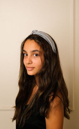 Young girl with long dark hair wearing a light gray headband against a plain background