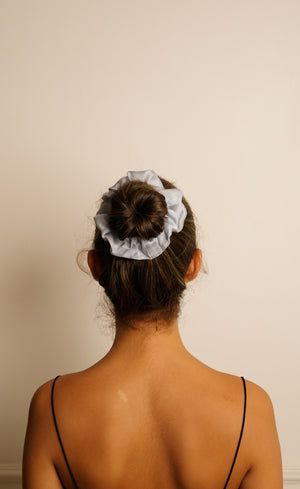 Person with a white scrunchie in their hair against a plain background