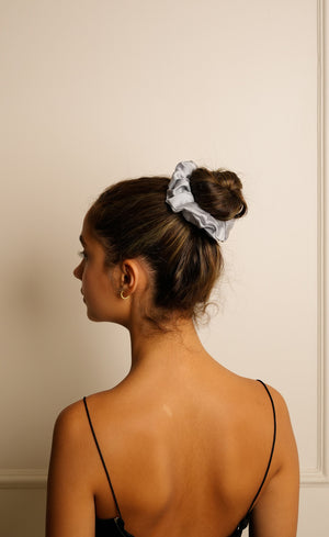 Woman with a scrunchie in her hair against a plain wall
