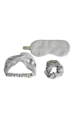 Set of silver eye mask, headband, and earbuds on a white background