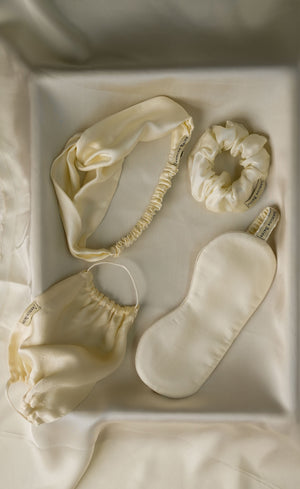 Set of cream-colored sleep accessories including a headband, eye mask, and scrunchie in a box.