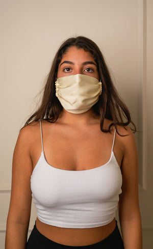 Woman wearing a beige face mask and white tank top against a plain background