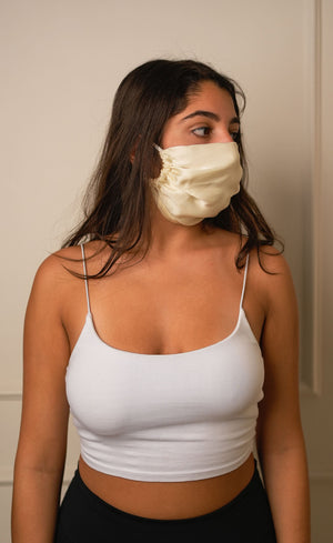 Woman wearing a white face mask and white tank top against a plain background