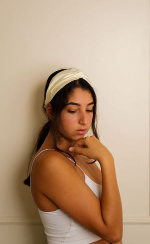 Woman wearing a white headband and tank top against a beige wall