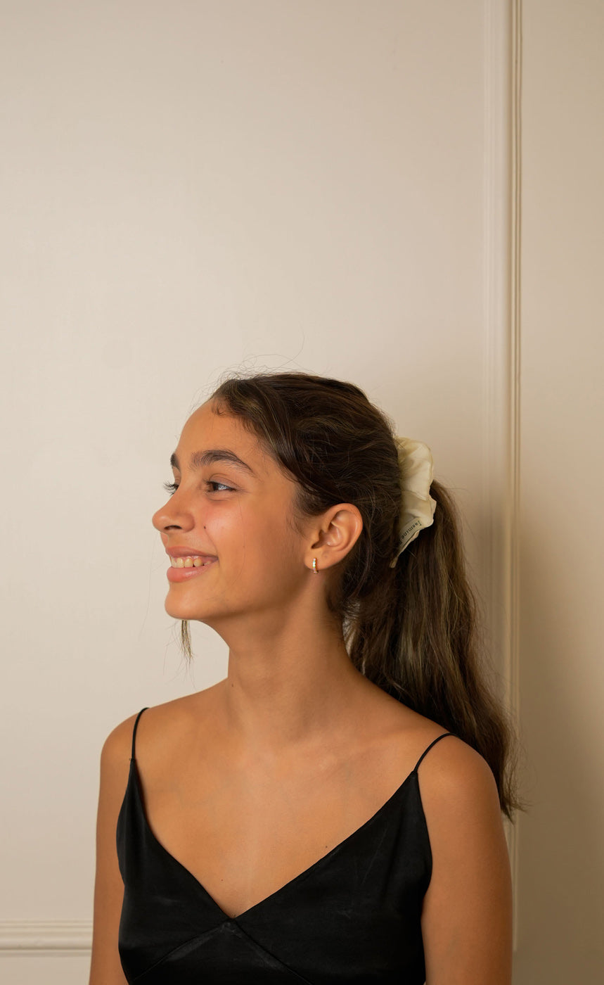 Woman with a ponytail wearing a white scrunchy against a neutral wall.