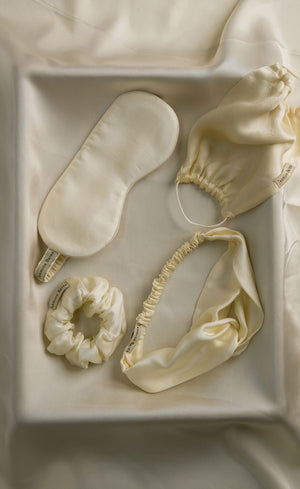 Set of cream-colored sleep accessories including a mask, headband, and scrunchie in a box.